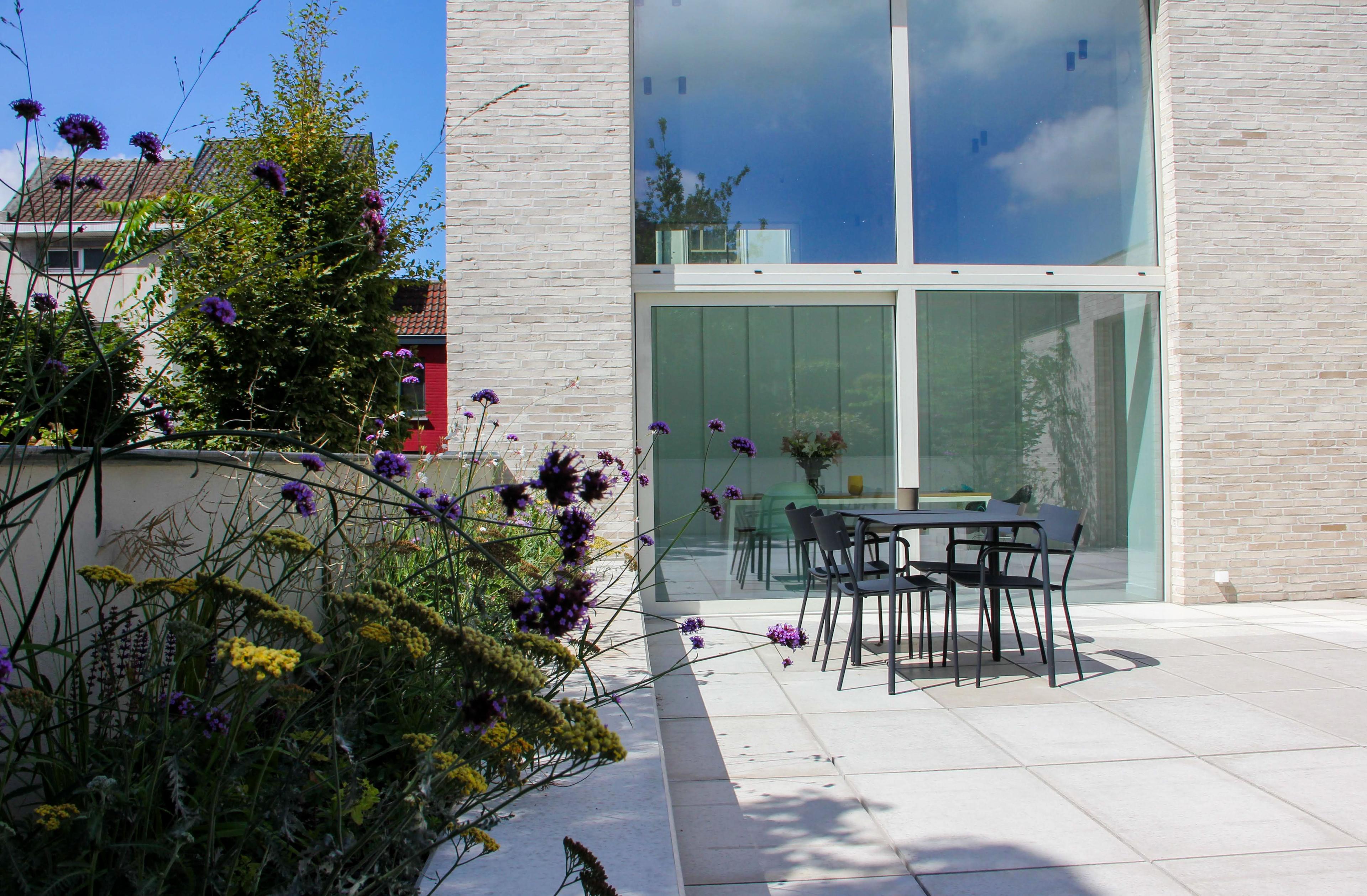 Zonnig terras met tuintafel voor de hoge glasgevel van de nieuwbouwwoning Nieuwland 28 in Gent.